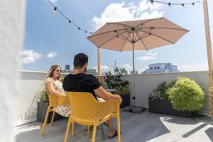 a man and woman sitting on a balcony with an umbrella at De' Mar Florentine Hotel By Peraia in Tel Aviv