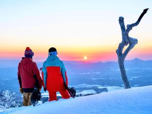 twee mensen die op een met sneeuw bedekte berg staan bij zonsondergang bij Palcall Tsumagoi Resort Ski & Hotel in Tsumagoi