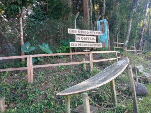 un banco de madera junto a un cartel en un bosque en Conjugado Aconchegante em Teresópolis, en Teresópolis