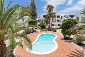 a swimming pool with palm trees and a building at Lanzahost Casa Cala in Costa Teguise