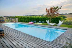 una piscina su una terrazza in legno con sedie intorno di En Marge a Aureville