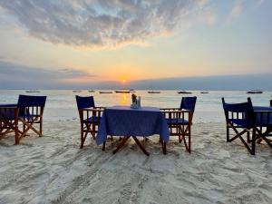uma mesa e cadeiras na praia com o pôr do sol em Zava Nungwi em Nungwi