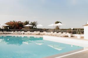 a swimming pool with white chairs and umbrellas at Hôtel Les Corallines – Thalasso & Spa in La Grande Motte