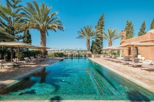 a pool with chairs and umbrellas and palm trees at Le Jardin des Douars in Ghazoua