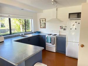 uma cozinha com armários azuis e um frigorífico branco em Hahei Beach House - 3 Bedroom em Hahei