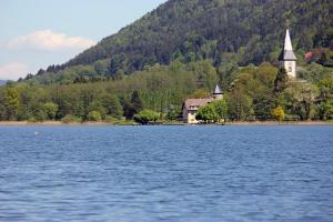 a lake with a church in the middle of a mountain at Ferienwohnung K+M+B am Ossiacher See - Jerry in Bodensdorf