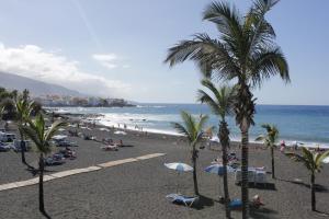a beach with people and palm trees and the ocean at Hotel Sun Holidays in Puerto de la Cruz