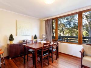 a dining room with a table and chairs and large windows at Gumtree Cottage Hawks Nest in Hawks Nest