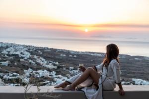 a woman sitting on a ledge watching the sunset at Nimbus Santorini in Oia