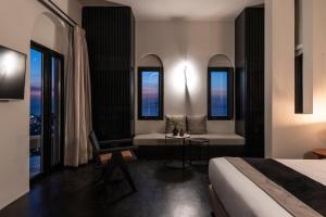 a hotel room with a bed and a couch and windows at Nimbus Santorini in Oia