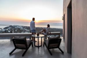 a man and a woman standing on a balcony with a table at Nimbus Santorini in Oia