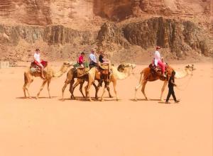 a group of people riding camels in the desert at Star City Camp wadirum in Wadi Rum