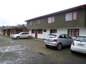 dos autos estacionados en un estacionamiento frente a un edificio en Hostal Fx, en Puerto Montt