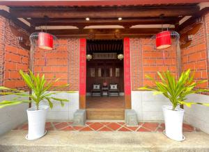 金門古寧歇心苑官宅古厝民宿 Guning Xiexinyuan Historical Inn في Jinning: مزرعتين في مزهريات بيضاء أمام المبنى