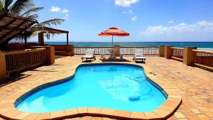 a swimming pool with an umbrella and chairs and the ocean at Vista do Mar in Inhambane