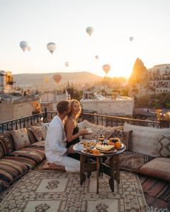 a man and woman sitting on a balcony with hot air balloons at Caftan Cave Suites in Göreme