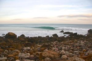 a rocky beach with a wave in the ocean at Pure Flor de Esteva in Vila do Bispo
