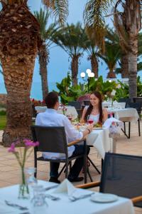 a man and woman sitting at tables at a restaurant at Queens Bay Hotel in Paphos