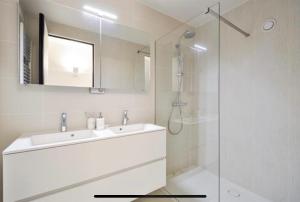 een witte badkamer met een wastafel en een douche bij Luxe appartement Arte, 50m van het Zoute strand in Knokke-Heist