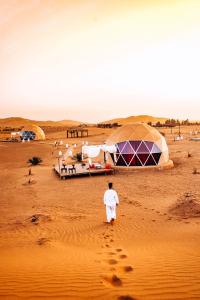 a man walking through the desert with tents and footprints at Sunrise Sahara Camp in Merzouga