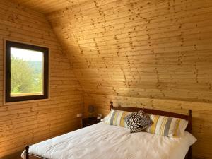uma cama num quarto de madeira com uma janela em Cabanele lu’ Dinu em Curtea de Argeş
