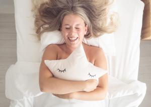 a woman laying in bed holding a pillow with eyes on it at Time Apartments Ylistönmäki in Jyväskylä