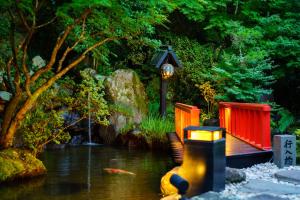 a pond with a bench and a bird house next to a river at Beppu Showaen in Beppu