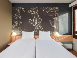 a bedroom with two beds and a wall with a drawing on it at ibis Charleroi Airport Brussels South in Charleroi