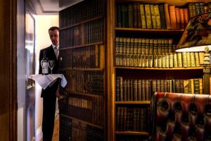 a man standing in a library with a bottle of wine at Dalhousie Castle Hotel in Bonnyrigg