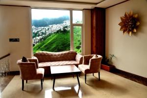 a living room with a couch and two chairs and a large window at The Orchid Hotel Shimla in Shimla