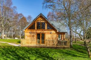 a log cabin with a large porch in the grass at Thistle Lodge 18 with Hot Tub in Belladrum