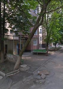 a tree in front of a building with a green bench at Квартира на бульваре Вечернем in Kryvyi Rih