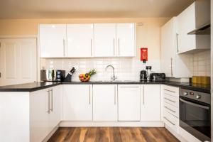 a kitchen with white cabinets and black counter tops at Emerald Court Executive Watford Central Apartment by PAY AS U STAY in Watford