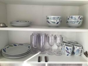 a shelf with plates and wine glasses and dishes at Cosy compact living with gym access. in Heberg