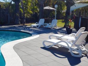 two lounge chairs and a swimming pool in a yard at Pacific Palms Motor Inn in Marcoola