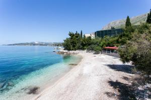 a beach with blue water and trees on a hill at Apartmani Kate, Plat in Mlini