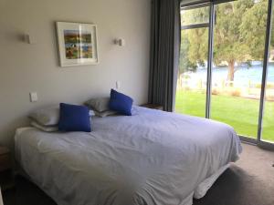 a bedroom with a bed with blue pillows and a window at Sunhaven Lakeside - Cromwell Holiday Home in Cromwell