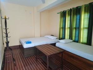 two beds in a room with a table and windows at Green Tree in Chitwan
