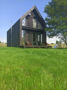 a house with two chairs in a field of grass at Między Olchami domek nad jeziorem. Noclegi całoroczne. Cisza, spokój. in Barczewo