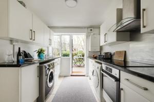 eine Küche mit weißen Schränken, einer Waschmaschine und einem Trockner in der Unterkunft Bright and Spacious Philbeach Garden Apartment in London