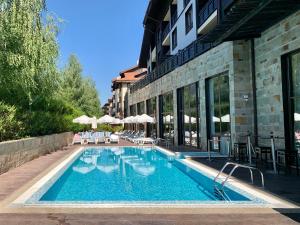 a swimming pool with chairs and umbrellas next to a building at Luxury Apartment Pirin Chalet in Terra Complex in Bansko