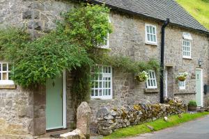 une maison en pierre avec une porte et des fenêtres vertes dans l'établissement Bankside Cottage, à Alstonfield