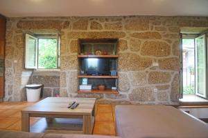 Habitación con pared de piedra, mesa y TV. en Casa Ze Rosa, en Gerês