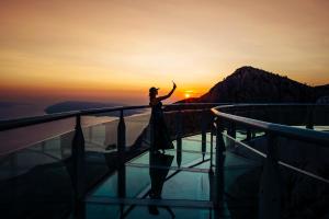 Eine Frau, die am Rand einer Aussichtsplattform bei Sonnenuntergang steht. in der Unterkunft Medora Auri Family Beach Resort in Podgora