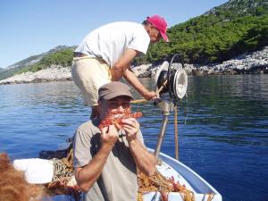 two men on a boat eating food in the water at Apartments Pitarević in Saplunara