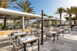 a restaurant with tables and chairs and palm trees at Hotel Riu Palace Maspalomas - Adults Only in Maspalomas