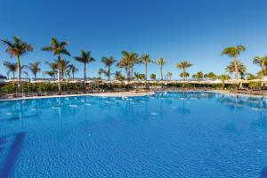 a large swimming pool with palm trees and umbrellas at Hotel Riu Palace Maspalomas - Adults Only in Maspalomas