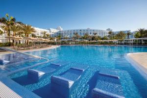 a large swimming pool in a resort with palm trees at Hotel Riu Palace Maspalomas - Adults Only in Maspalomas