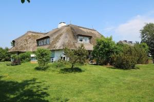 a thatched house with a grass roof on a field at Teewelkenhues-Wiesenappartement in Archsum