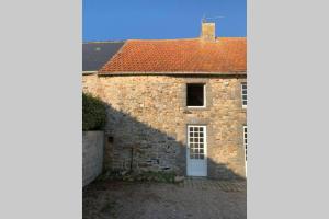 Casa de piedra con puerta blanca y techo rojo en SCIOTOT - Bord de mer - La petite maison, en Les Pieux